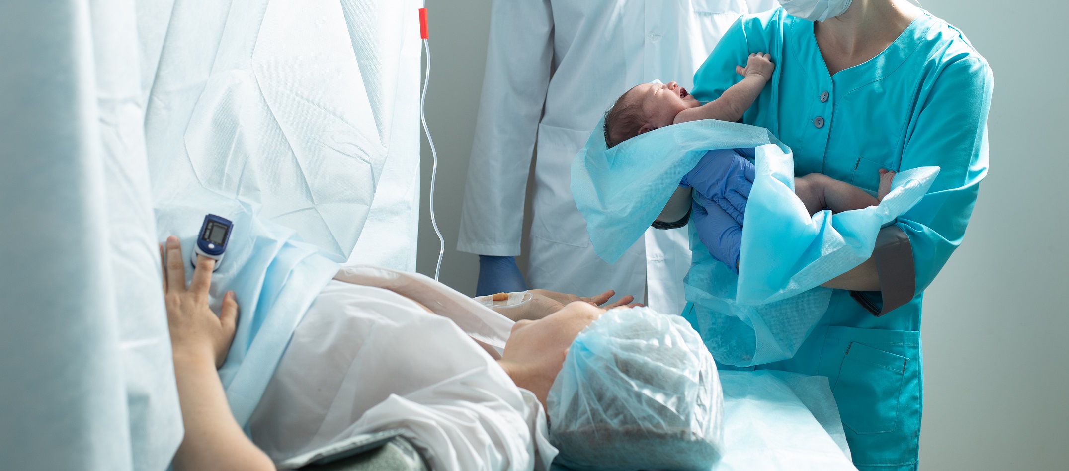 Nurse holds newborn baby close to mother in hospital